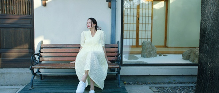 A person in a white dress sitting on a bench

Description automatically generated