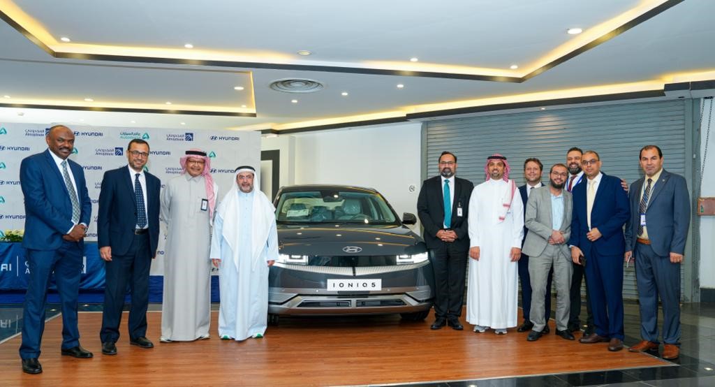 A group of men standing in front of a car

Description automatically generated